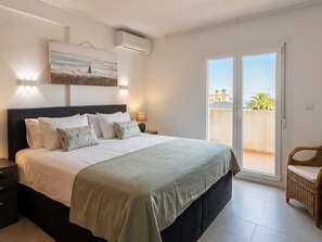 Ein Schlafzimmer mit Bett, Nachttischen, einer Wand-Klimaanlage, einem Fenster und einem Balkon mit Stuhl.