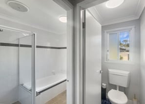Een badkamer met douche, toilet en raam.