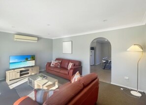 Een moderne woonkamer met een flatscreen televisie, een rode bank, een salontafel en een lamp.
