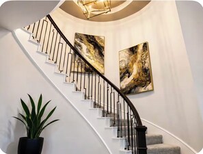 A curved staircase with black railings and white steps, flanked by two abstract paintings. - Luxury Living  (Pattison)