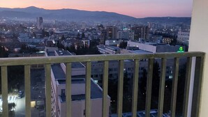 Un paisaje urbano al anochecer, con edificios y una cadena montañosa distante.