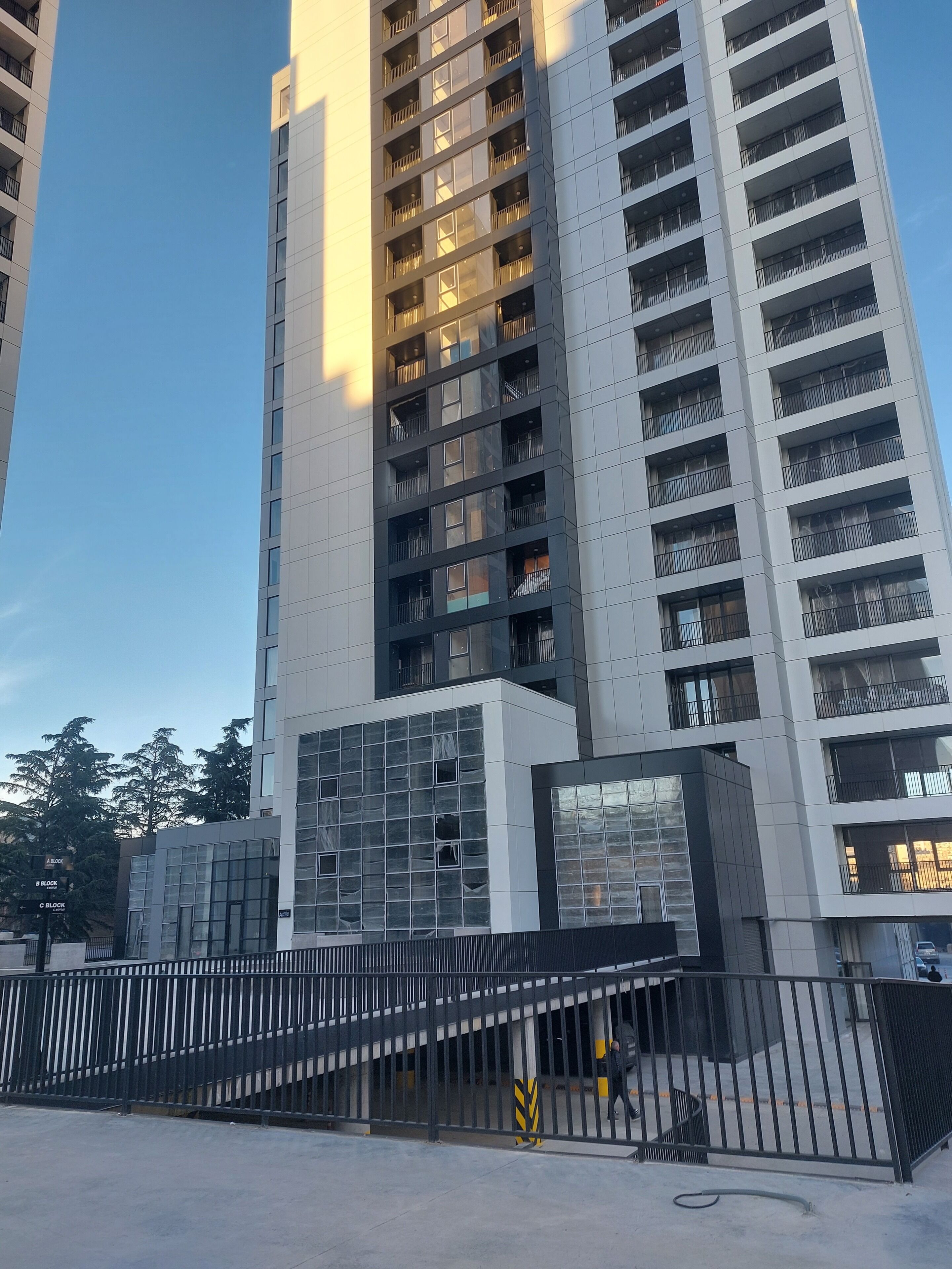 A high-rise building with multiple balconies, a gated entrance, and a stairway leading to the entrance.