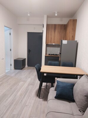 Et moderne køkken med træskabe, et køleskab og en komfur. Der er et spiseområde med et bord og stole, og en sofa med puder.
