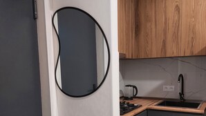 Una cocina moderna con armarios oscuros, encimera de madera, espejo circular negro y estufa empotrada.