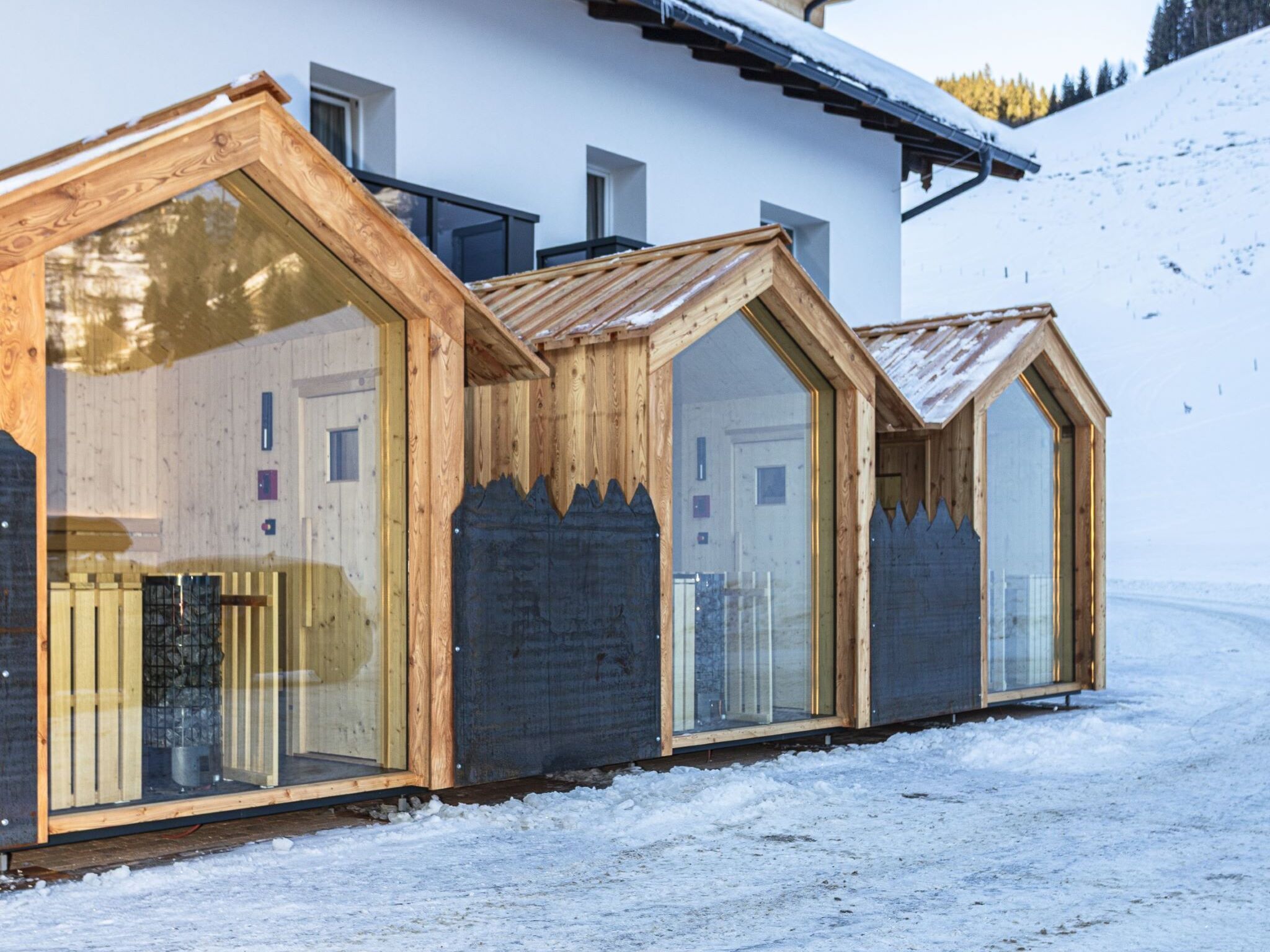 A row of wooden cabins with large windows, set against a snowy backdrop.