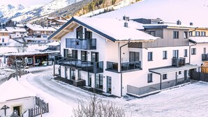 A modern ski resort building with multiple floors, large windows, and a snow-covered landscape in the background. - Dreamy apartment right by the slope (Hinterglemm)