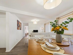 Ein modernes Esszimmer mit einem Holztisch, der für eine Mahlzeit gedeckt ist, einer Couch im Hintergrund und einer Vase mit Blumen auf dem Tisch.