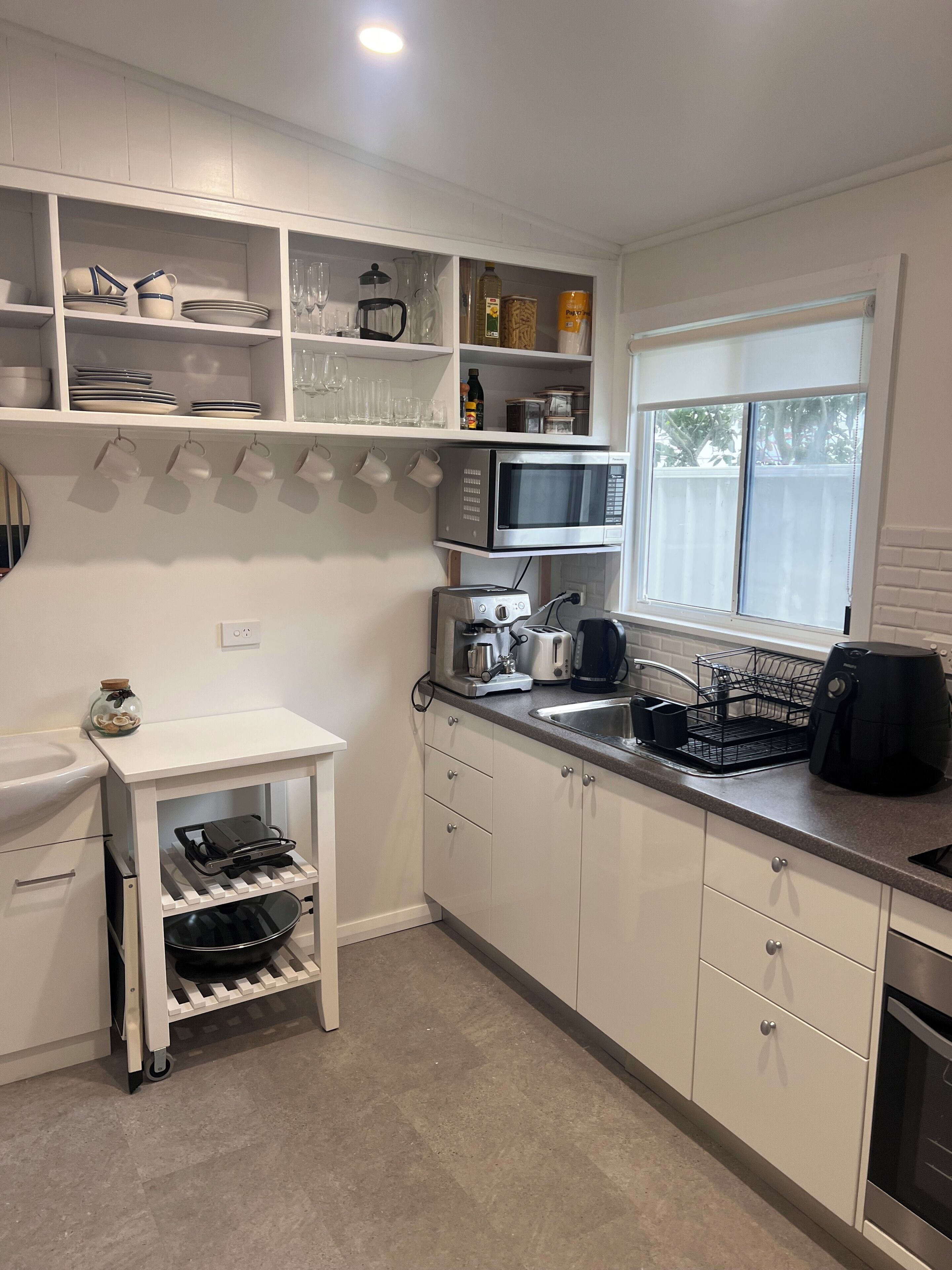 Una cocina moderna con armarios blancos, microondas integrado, cafetera y espacio para vinos.