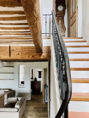 A staircase with a wooden handrail, a clock, and a view into a room with a sofa and a door leading to another room.