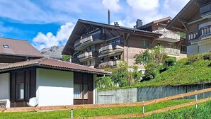 Ein Wohngebäude mit mehreren Balkonen, einem geneigten Dach und Blick auf Berge im Hintergrund.