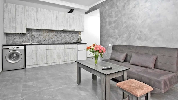 Una cocina moderna con armarios grises, una lavadora y un sofá gris en una sala de estar con pared texturizada en gris.