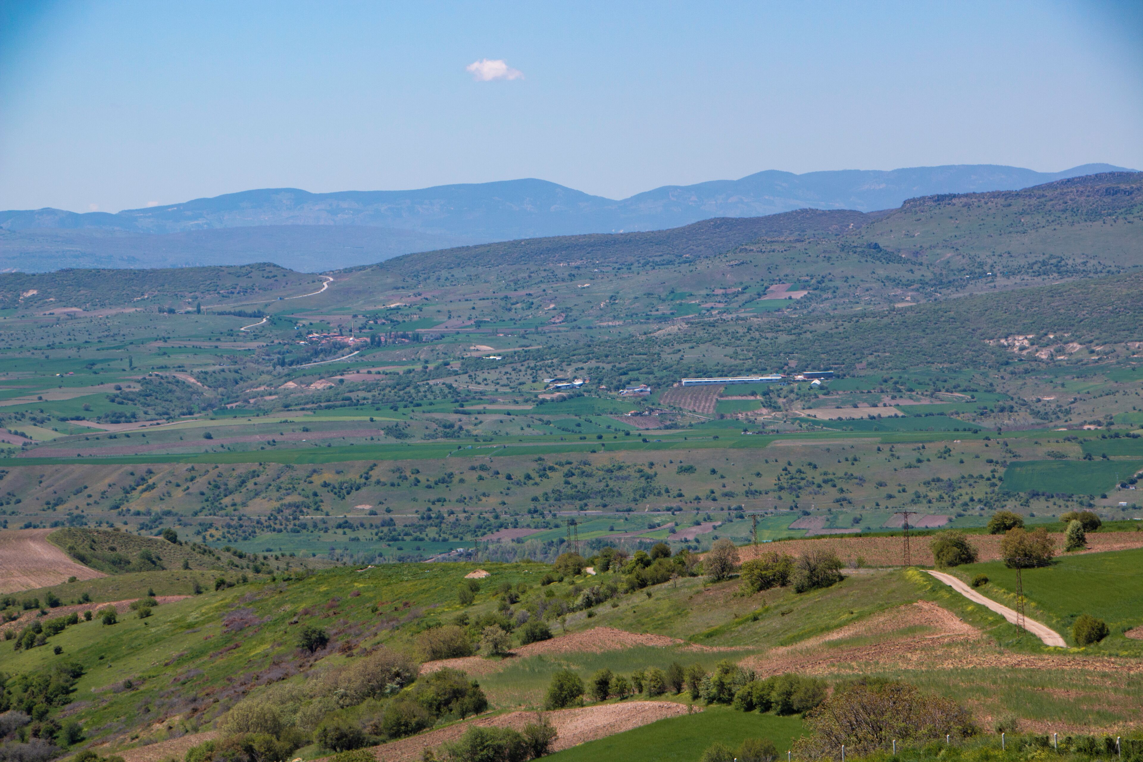 A panoramic view of a hilly landscape with fields, a winding road, and distant mountains.