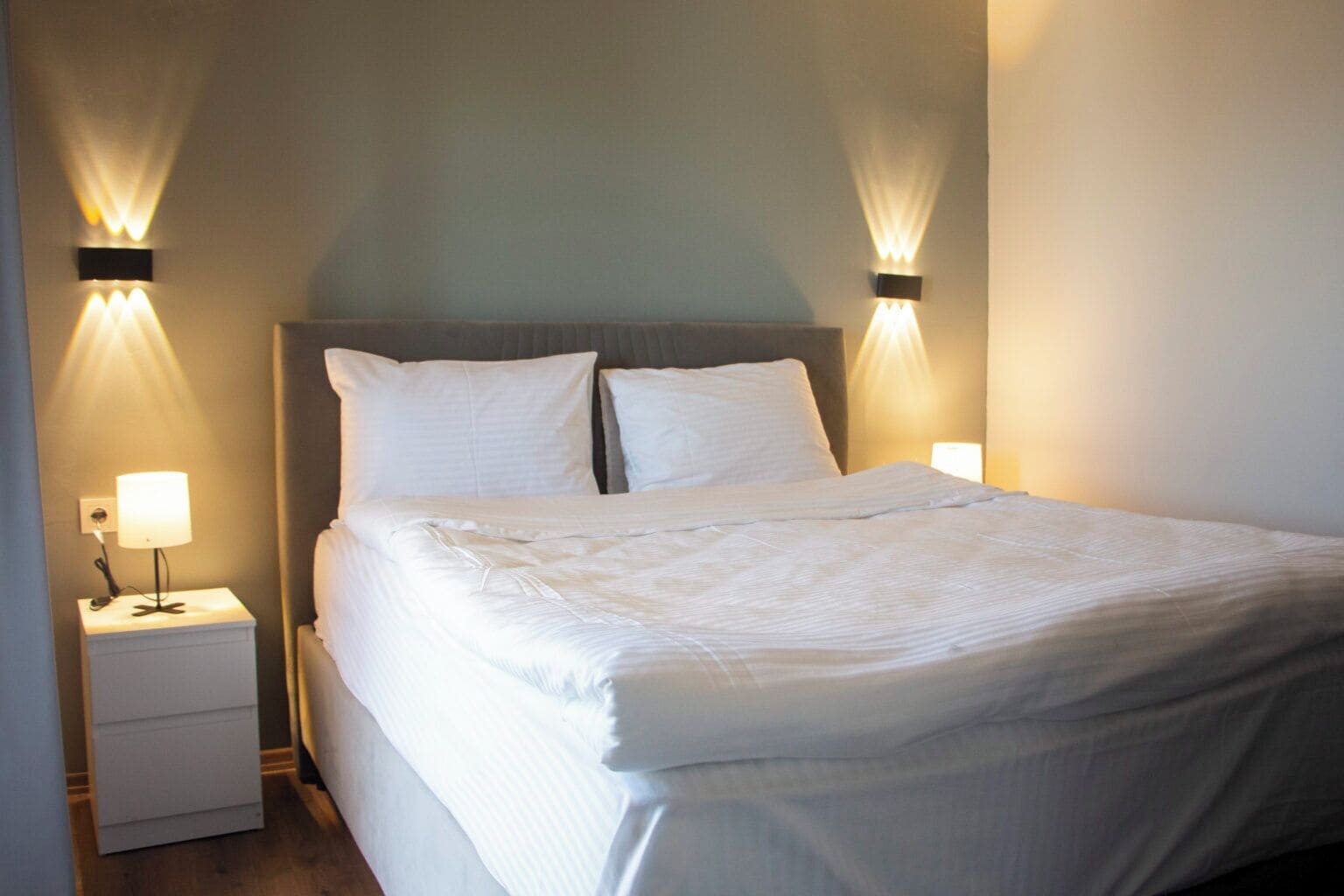A neatly made bed with white linens, a headboard, and two bedside lamps on a nightstand.