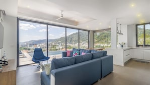 Un salon moderne avec un canapé, un fauteuil et une vue sur le paysage urbain, visible à travers de grandes fenêtres.