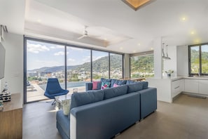 Ein modernes Wohnzimmer mit einer Couch, einem Sessel und Blick auf eine Skyline durch große Fenster.