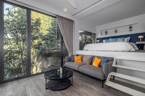 Ein modernes Hotelzimmer mit großem Fenster, einer Couch, einem Bett und einem kleinen Tisch.