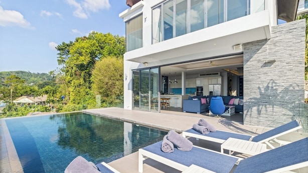 Une maison moderne dotée d’une piscine, de chaises longues et offrant une vue sur la verdure environnante.