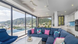 Un salon moderne avec un grand canapé, une table basse et une vue sur la ville et les montagnes, grâce à de grandes fenêtres.