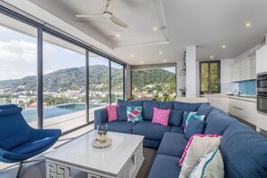 Ein modernes Wohnzimmer mit einem großen Sofa, einem Couchtisch und Blick auf eine Stadt und Berge durch große Fenster.