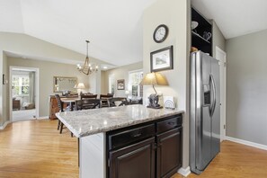 A kitchen with a stainless steel refrigerator, a marble countertop, and a dining area with a chandelier. - Kick App VIEWS! Mt Cabin w/Hot Tub +Fireplace (Seven Devils)