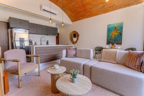 Ein modernes Wohnzimmer mit einer Couch, einem Holzstuhl, einem Couchtisch und einer Küchenzeile im Hintergrund.