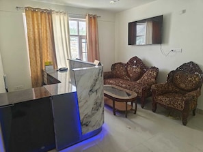 Uma sala de estar com uma receção em mármore, sofás estampados, uma televisão e uma janela com cortinas.
