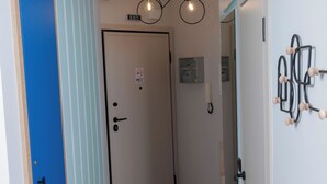 Un couloir avec une porte bleue, une porte blanche avec une pancarte et un luminaire.