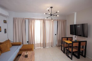 Una sala de estar con un sofá, una mesa de madera, un televisor montado en la pared y una lámpara en el techo.