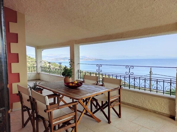 Ein Balkon mit Tisch, Stühlen, einer Topfpflanze und Blick aufs Meer.