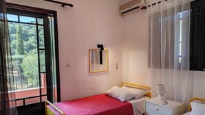 Ein Schlafzimmer mit zwei Betten, einem Fenster mit Blick auf Grünflächen, einem Spiegel und einem Nachttisch mit Lampe.