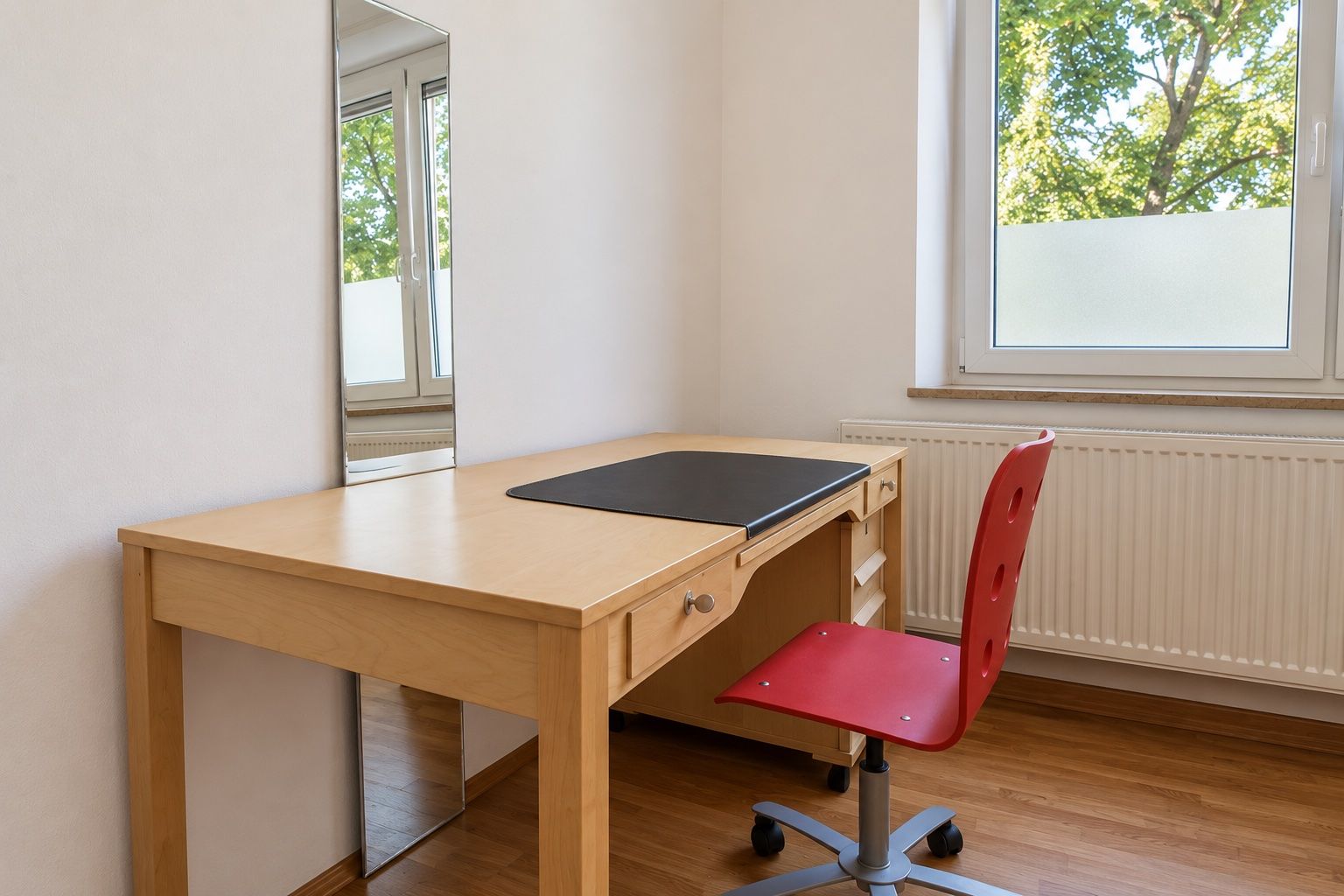 A room with a wooden desk, a red chair, a mirror, and a window with a view of trees.