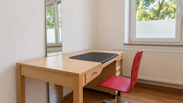 A room with a wooden desk, a red chair, a mirror, and a window with a view of trees.