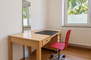 A room with a wooden desk, a red chair, a mirror, and a window with a view of trees. - New Leonrod  · Big groups Oktoberfest (MÃ¼nchen)