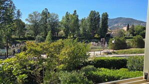 A view of a lush garden with various trees and shrubs, a pathway, and a distant mountain. - The Golf Studio. Swimming pool, close to beach, walks, golf course, shops and restaurants. (Mandelieu-la-Napoule)