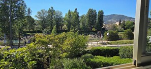 A view of a lush garden with various trees and shrubs, a pathway, and a distant mountain. - The Golf Studio. Swimming pool, close to beach, walks, golf course, shops and restaurants. (Mandelieu-la-Napoule)