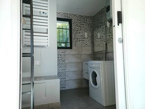 A laundry room with a washing machine, a drying rack, and a window with a view of greenery. - Nestled in a park, in a typical Provencal neighborhood of villas, near mourillon (Toulon)
