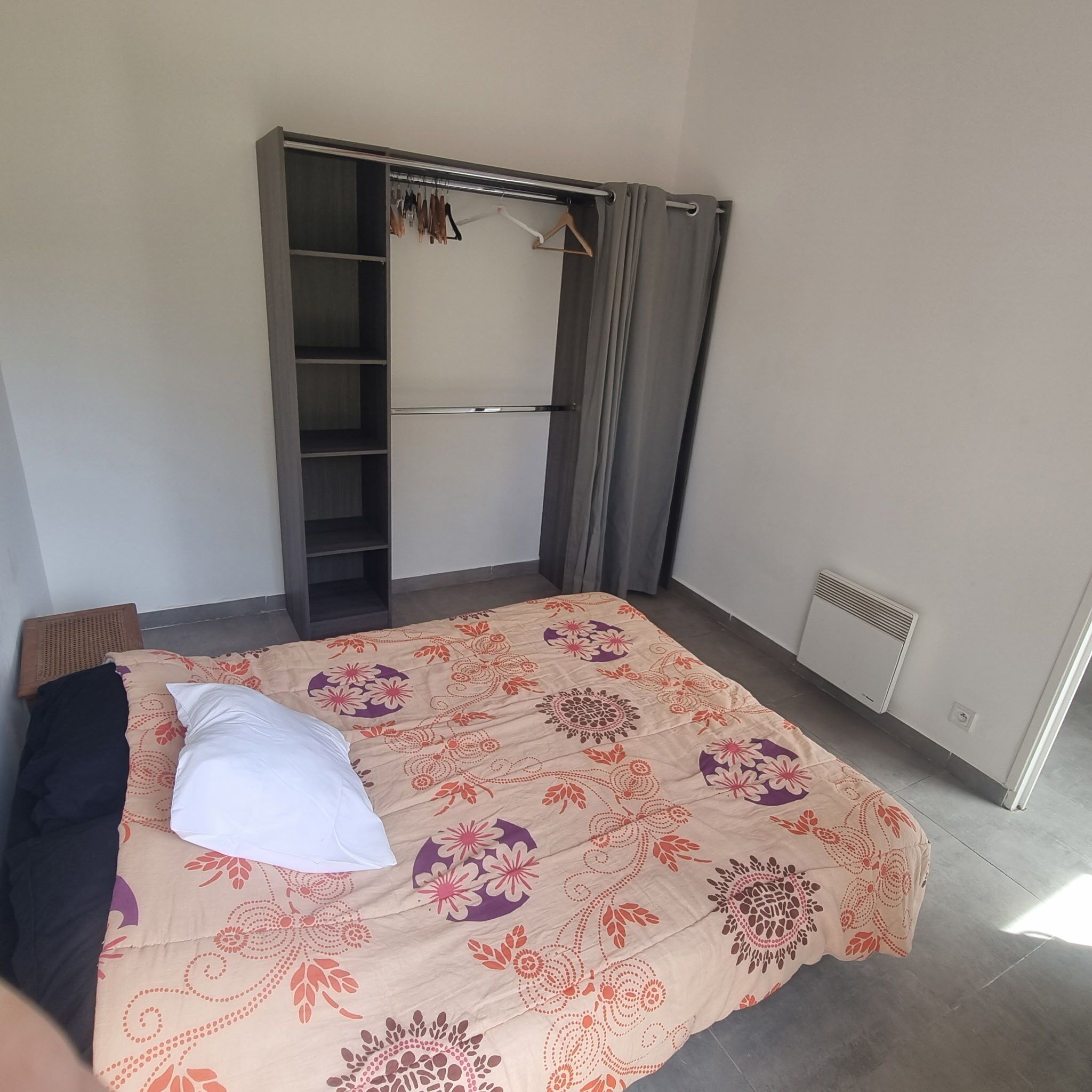 Une chambre à coucher comprenant un lit, une armoire, un portant et un radiateur.