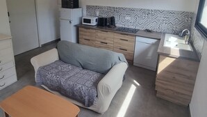 Ett kompakt kök med mikrovågsugn, kaffebryggare och diskmaskin. I vardagsrummet finns en soffa och ett träbord.