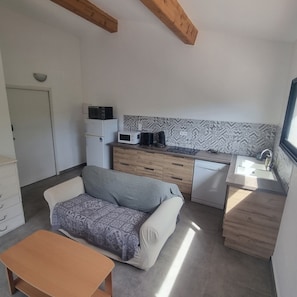 A compact kitchen with a microwave, coffee maker, and dishwasher. There's a sofa and a wooden table in the living area. - Nestled in a park, in a typical Provencal neighborhood of villas, near mourillon (Toulon)