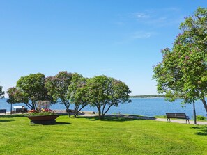 A park with a grassy area, benches, and trees by a body of water.