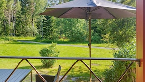 Um terraço com móveis de exterior, uma pérgula e vista para uma área gramada com árvores.