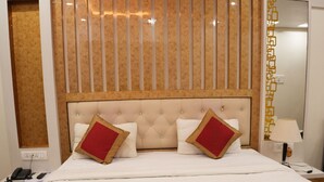 A hotel room with a large bed, a headboard with vertical slats, a bedside table with a lamp, and a mirror on the wall. - Aradhaya Heritage Hotel (Bodh Gaya)
