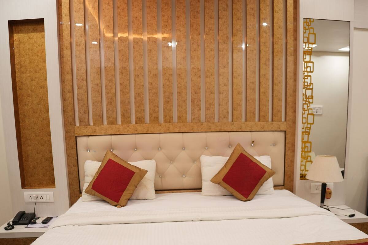 Habitación de hotel con una cama grande, cabecero con listones verticales, mesita de noche con lámpara y un espejo en la pared.
