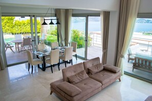 Ein modernes Wohnzimmer mit einer Couch, einem Esstisch, Stühlen und großen Glasüren, die auf einen Balkon mit Meerblick führen.