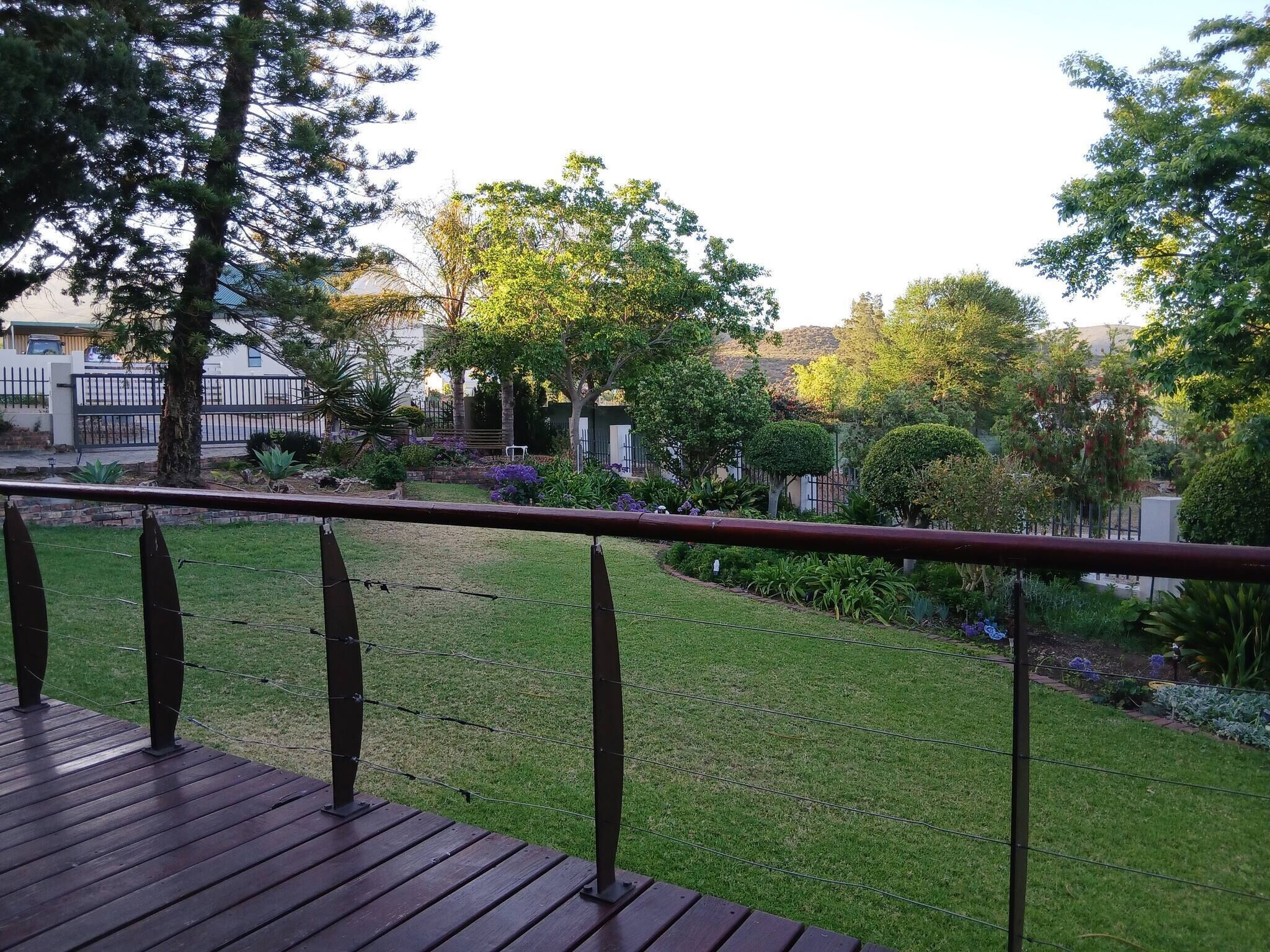Une terrasse dotée d’une rambarde en métal, qui offre une vue sur un jardin bien entretenu, agrémenté de diverses plantes et arbres.