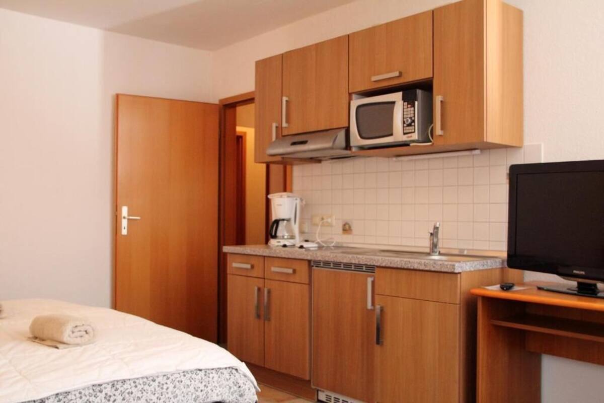 A compact kitchen with wooden cabinets, a microwave, a coffee maker, and a television.