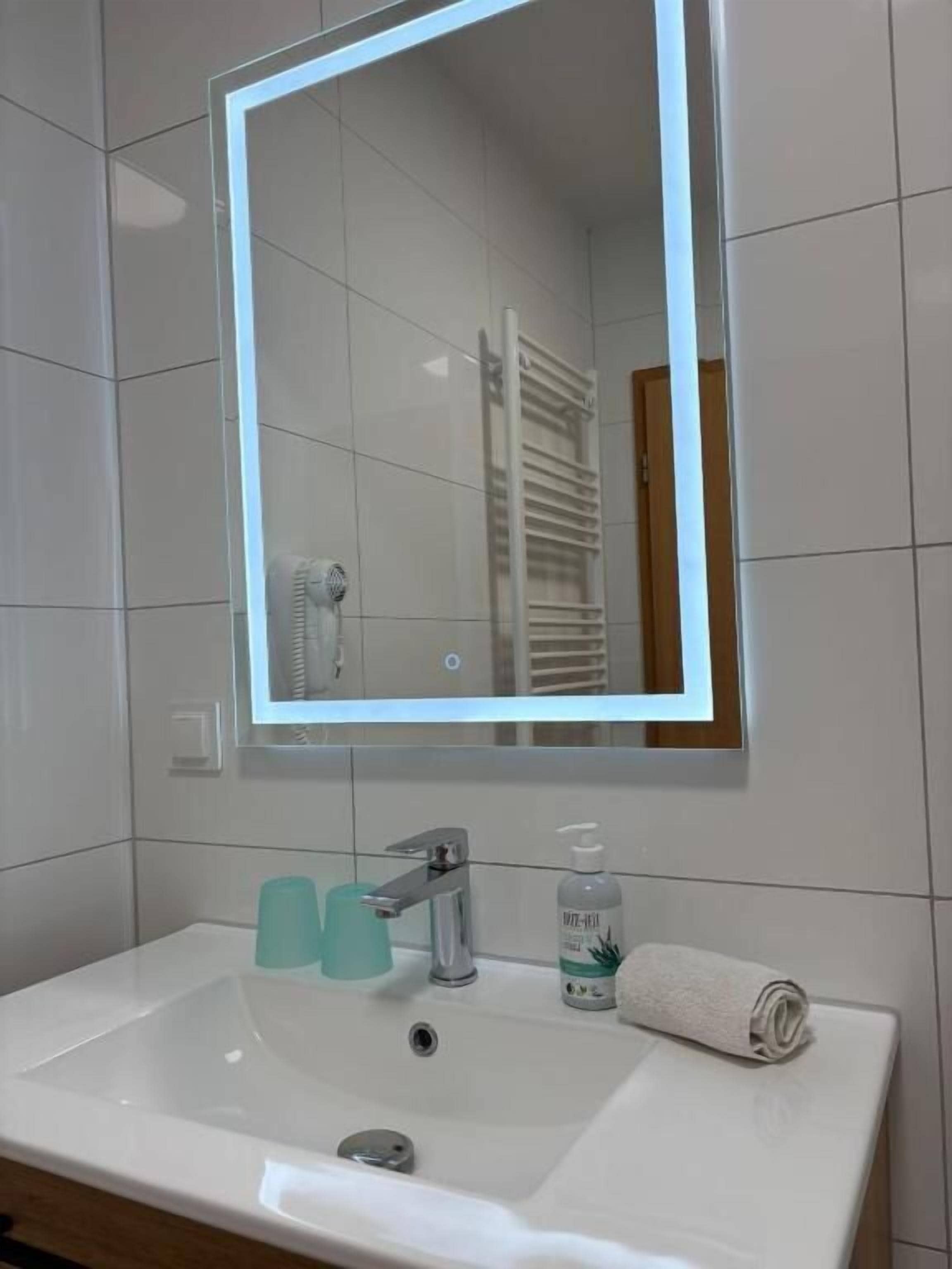 A bathroom with a white sink, a mirror, a towel, and a bottle of hand soap.