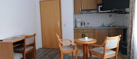 Ein gemütliches Hotelzimmer mit Bett, Schreibtisch, zwei Stühlen, einem kleinen runden Tisch, einem Fernseher und einer Küchenzeile.