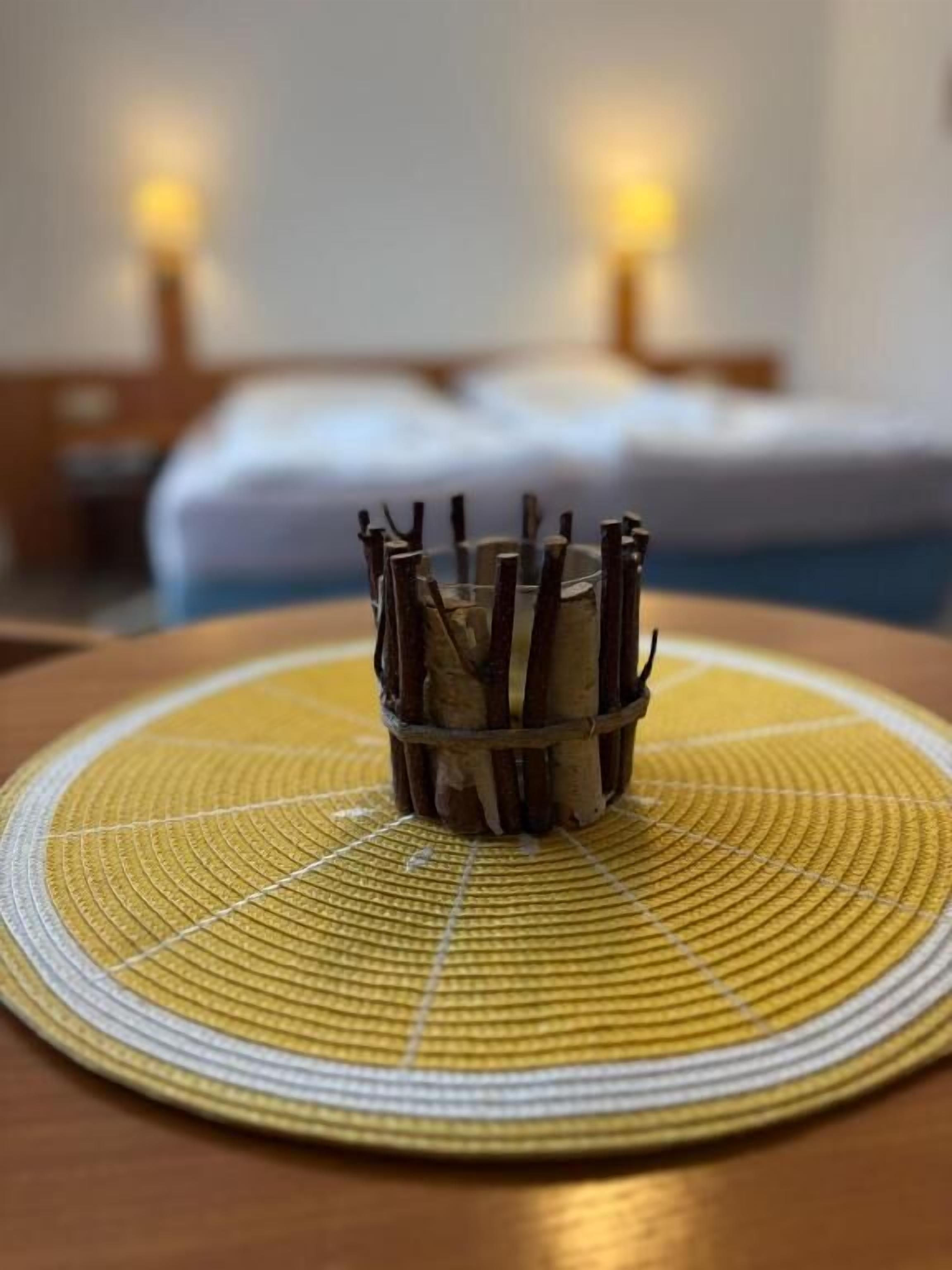 A circular woven placemat with a central woven basket containing sticks.