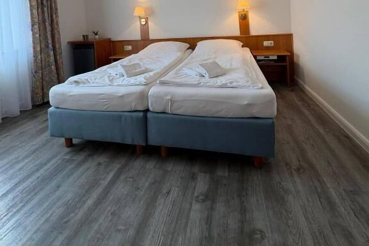 A double bed with a wooden headboard, two bedside tables, a clock, and a ceiling light fixture.